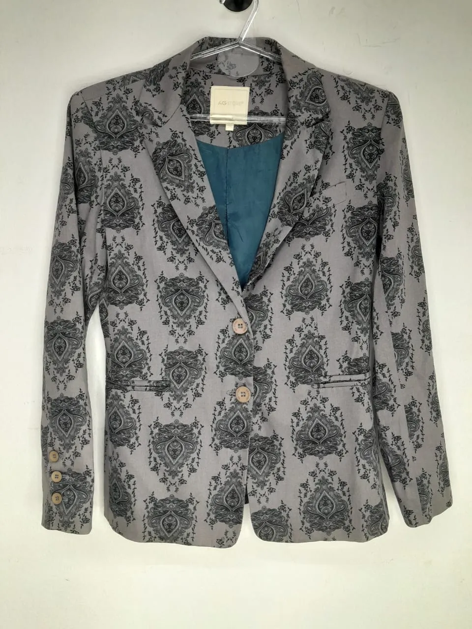 Blazer gris con estampado floral en negro. Tiene dos botones al frente y puños con botones.