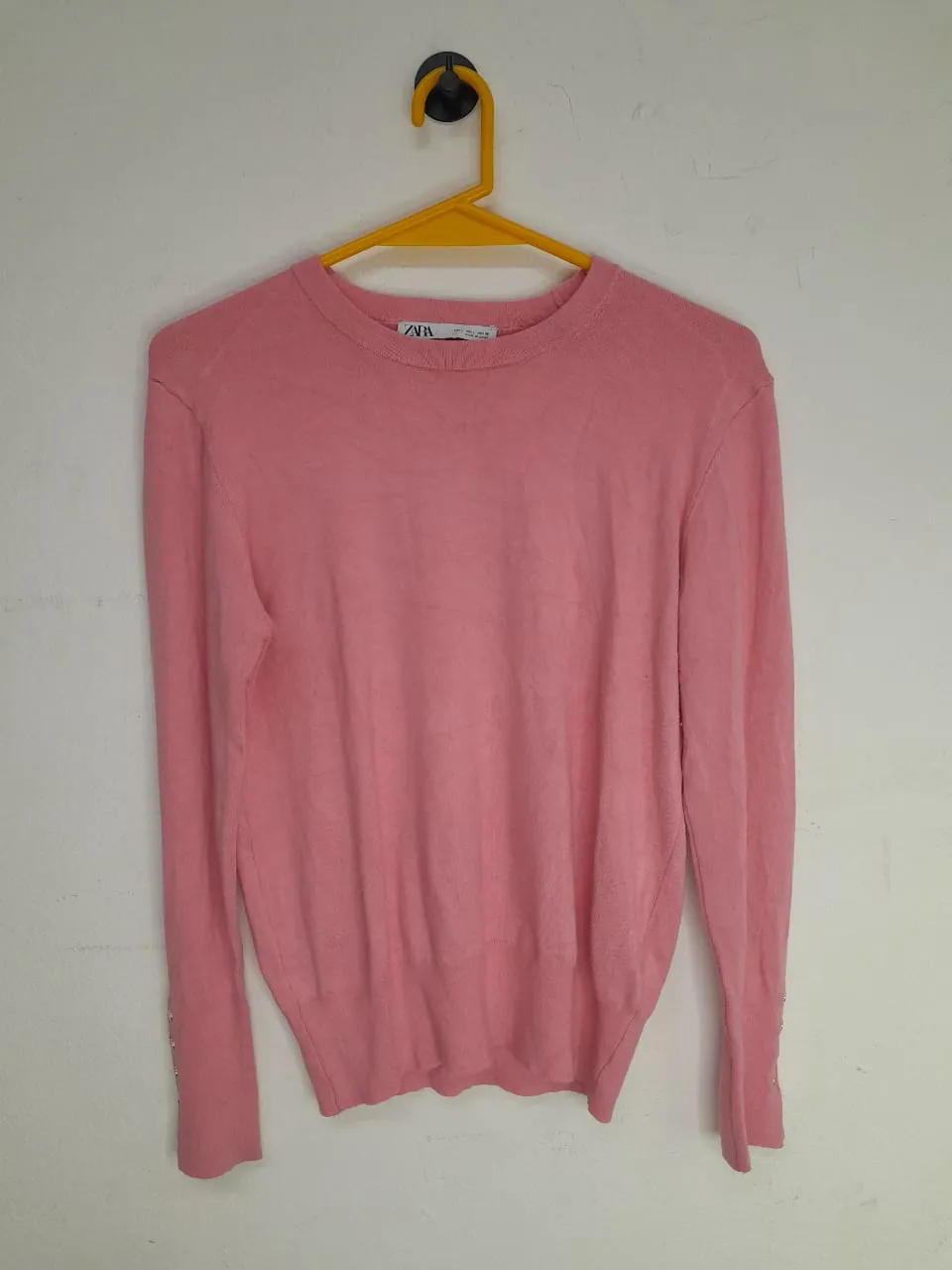 Sweater rosa de manga larga con cuello redondo. Posee botones decorativos en los puños.