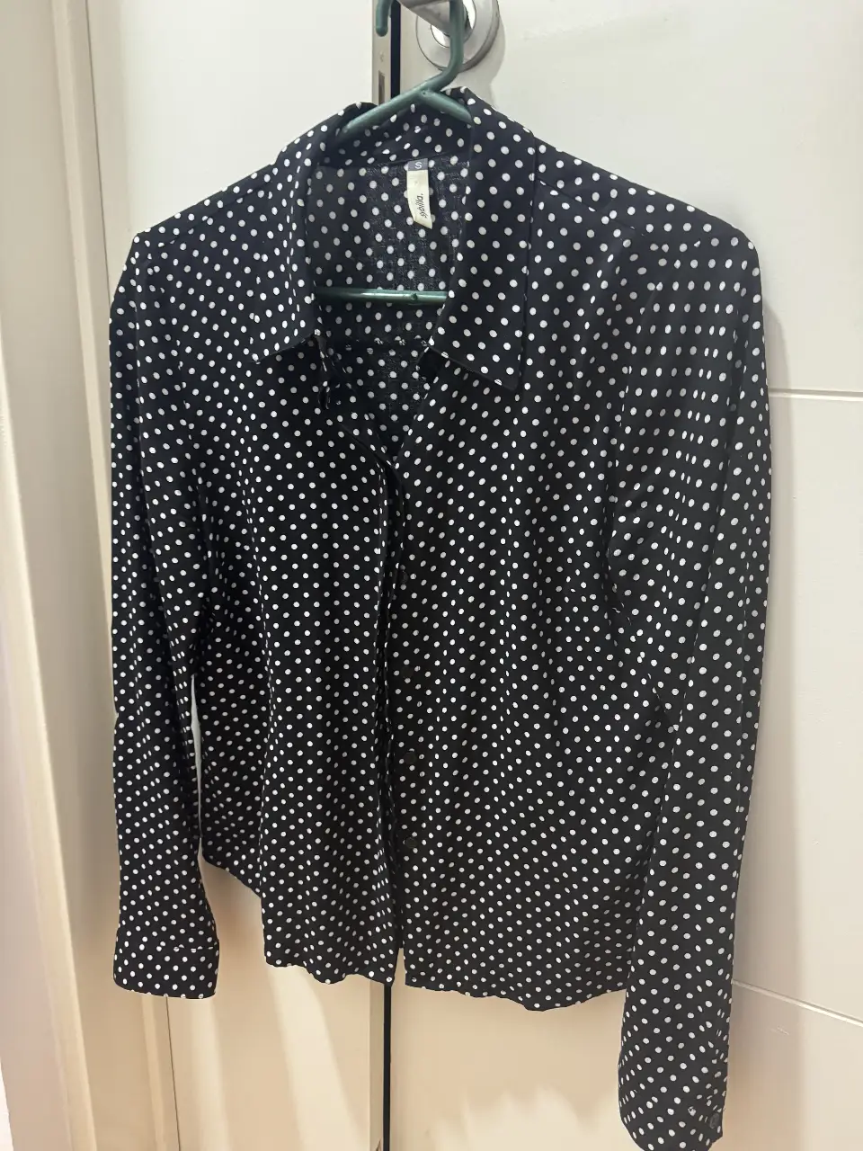 Camisa de mujer con estampado de lunares blancos sobre fondo negro. Cuello camisero y mangas largas. Ideal para un look elegante y versátil.