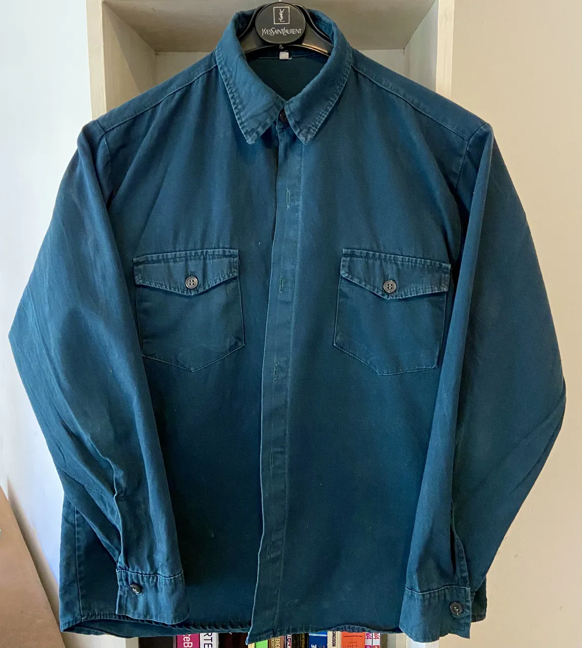 Camisa de manga larga de color azul oscuro, con cuello clásico y dos bolsillos en el frente. Perfecta para un look casual o de trabajo. Está ligeramente gastada por uso.