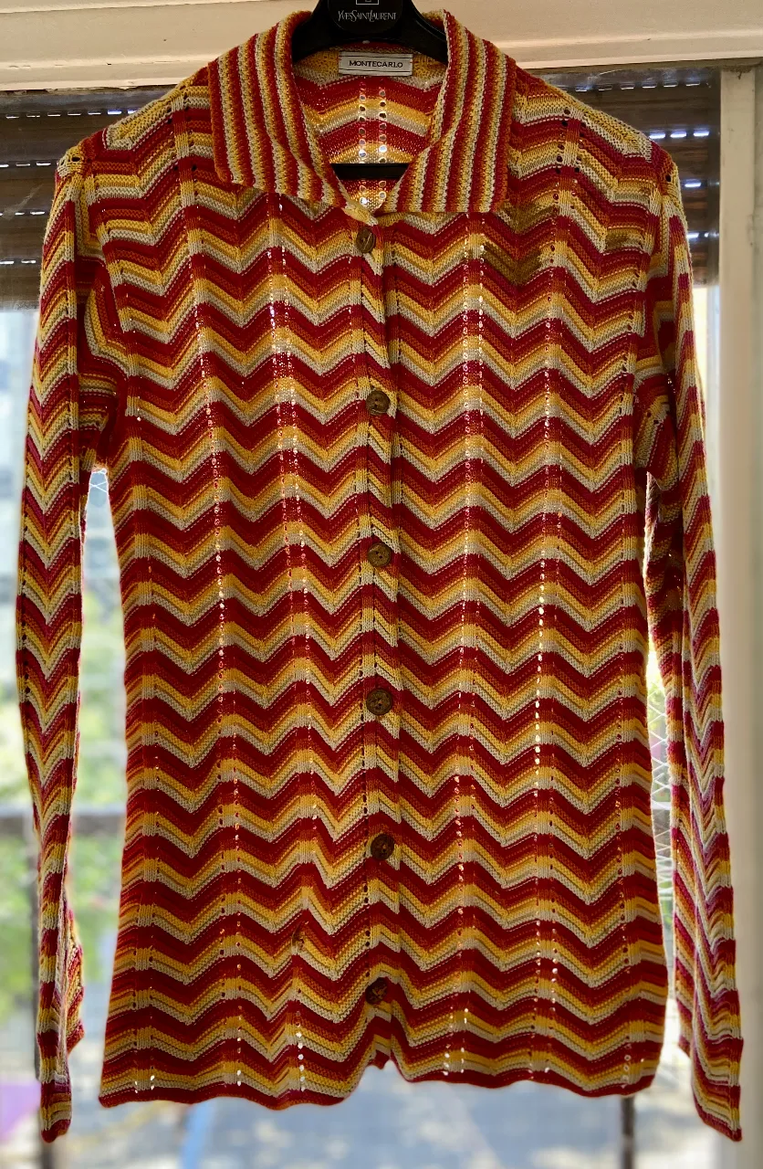 Camisa tejida a crochet con un vibrante diseño de zig-zag en tonos rojos, amarillos y blancos. Posee cuello camisero y botones al frente. Ideal para un look retro y canchero.
