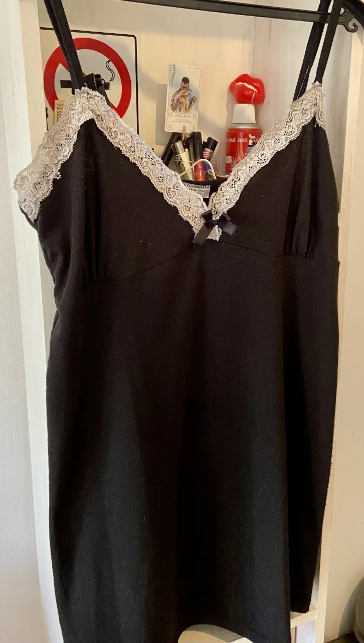 Vestido negro de algodón con detalles de encaje blanco en el escote y tiras finas. Tiene un pequeño moño en el centro del busto. Se generaron pelotitas en su mayoría del lado derecho del vestido por uso. 