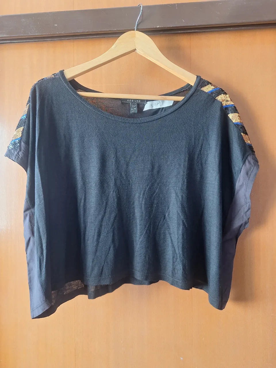 Remera negra corta con detalles de lentejuelas doradas, negras y azules en los hombros.