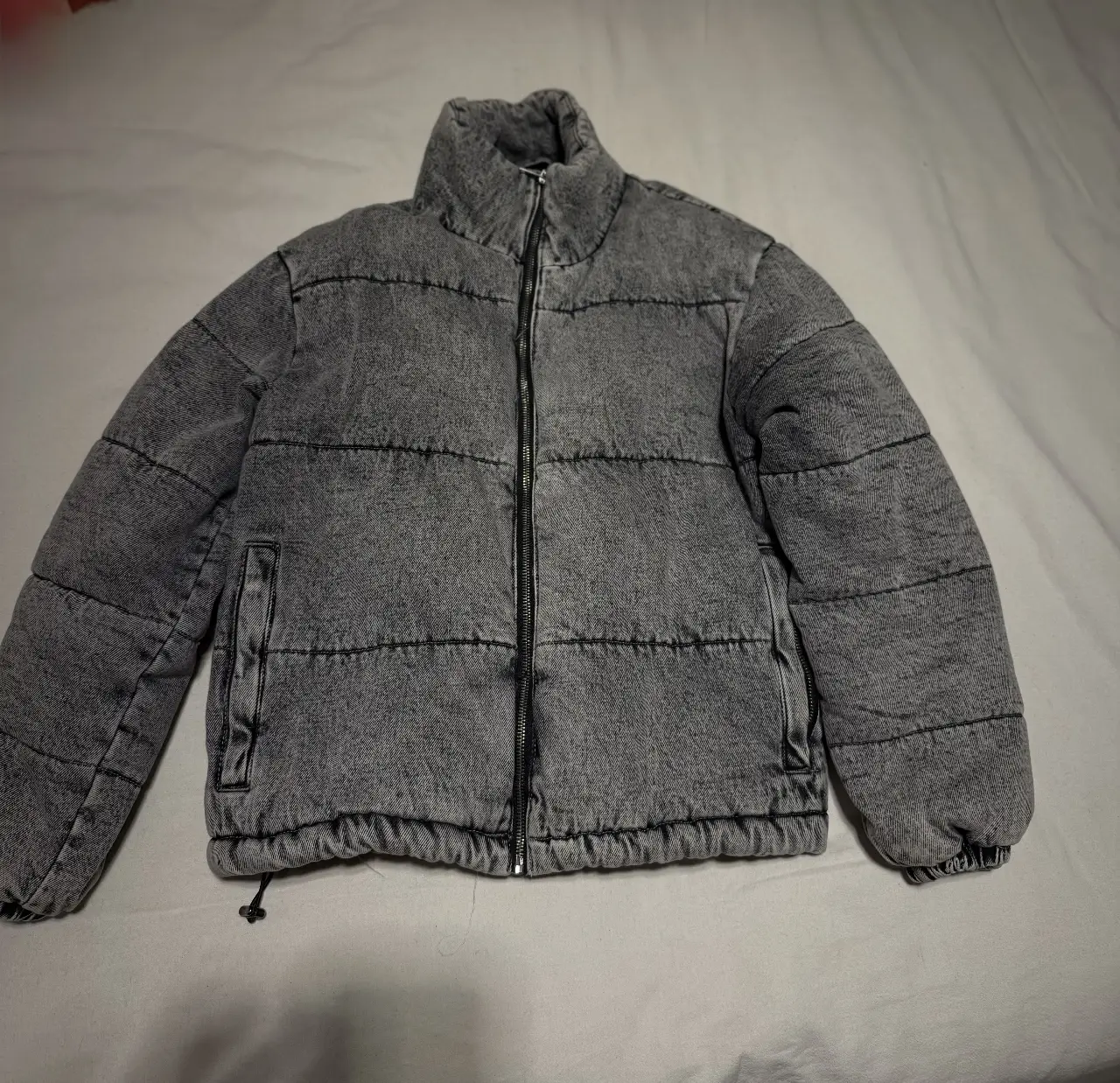 Campera puffer gris con cierre frontal y cuello alto. Ideal para un look casual y abrigado en invierno. Perfecta para combinar con jeans o pantalones.