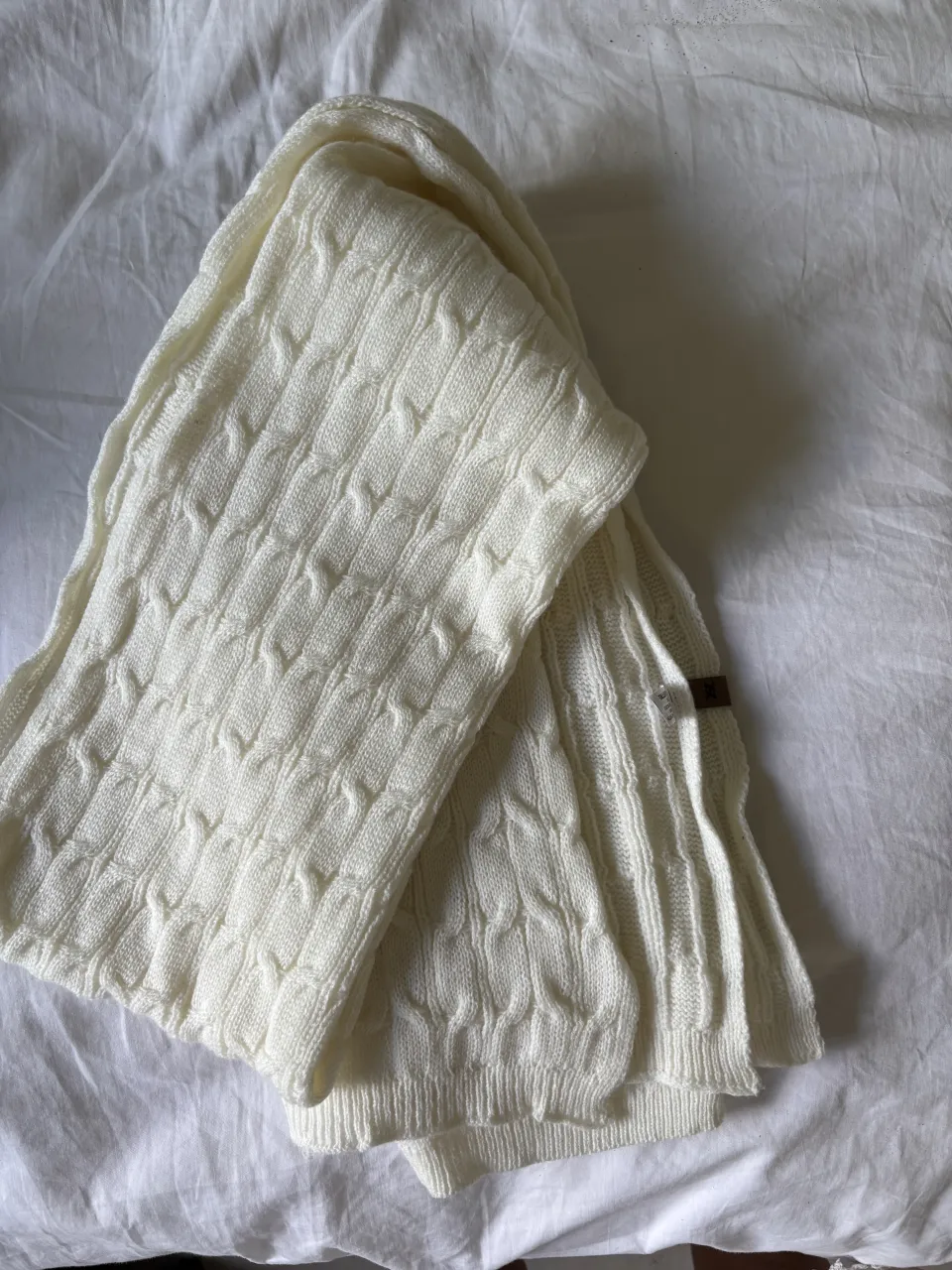 Bufanda tejida color blanco con diseño de trenzas. Posee una etiqueta de marca marrón.