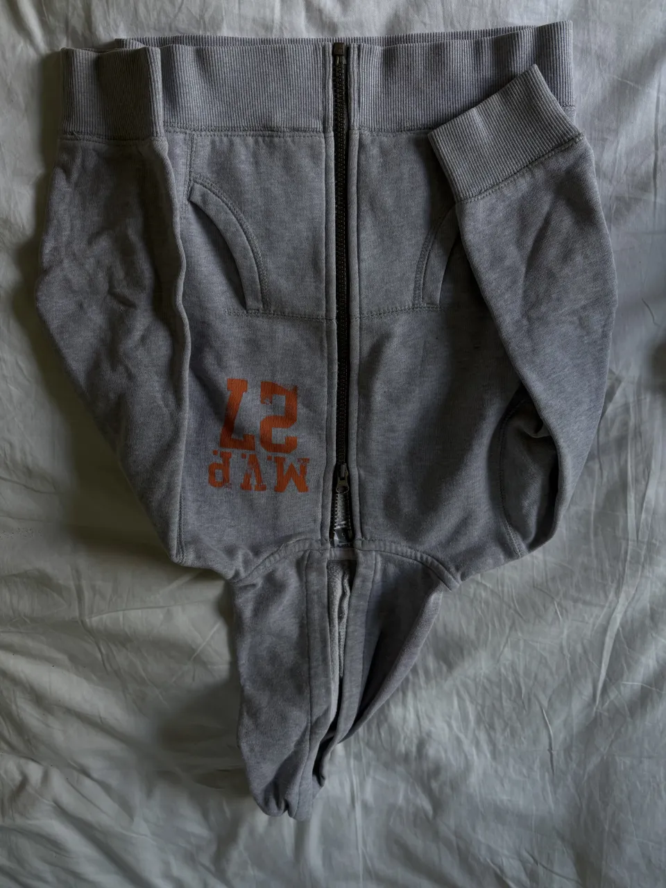 Buzo gris con cierre completo y estampa naranja "MVP 27" en el frente. Tiene bolsillos tipo canguro.