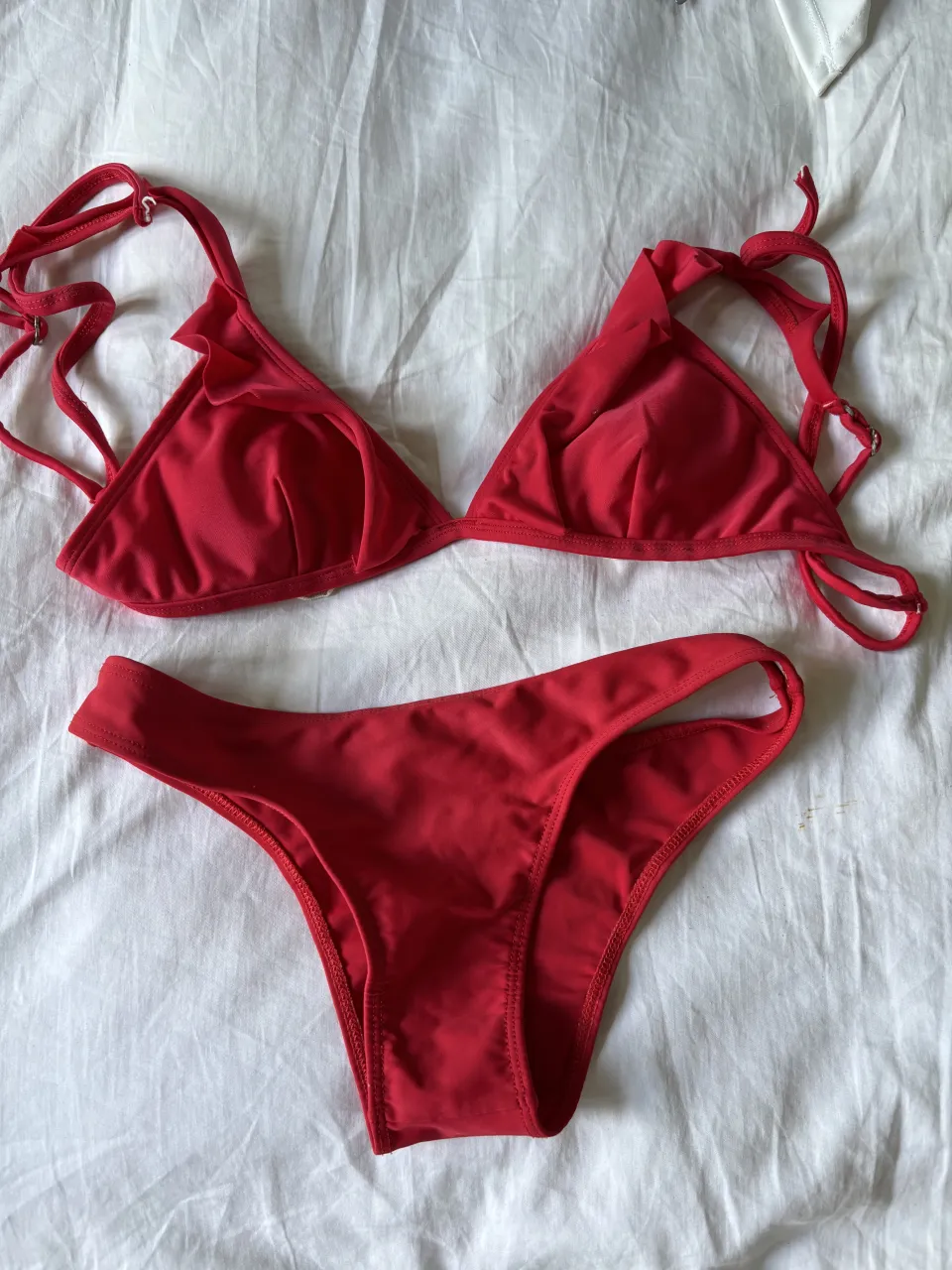 Bikini roja de dos piezas. El corpiño es triangular con volados y tiras para atar en cuello y espalda. La bombacha es estilo colaless.