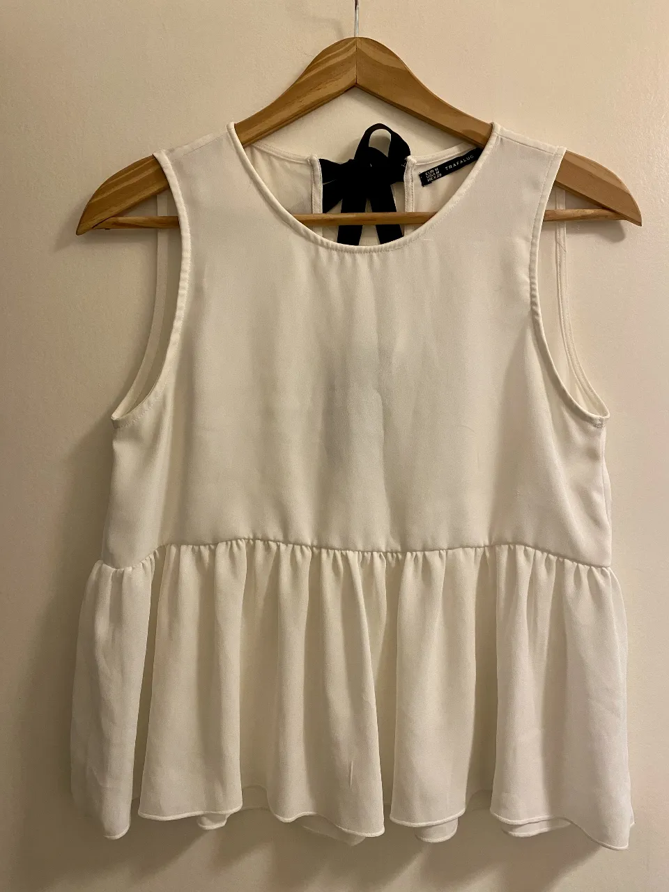 Blusa blanca con detalle de lazo negro en la espalda. Corte holgado y peplum en la parte inferior. Ideal para un look elegante y fresco.