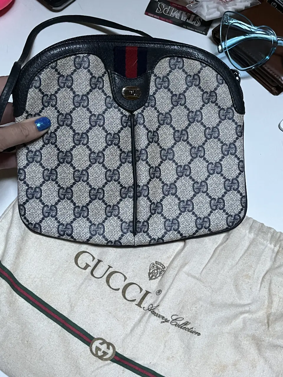 Cartera Gucci vintage con el icónico estampado GG. Diseño bandolera con detalles en cuero negro y la clásica cinta tricolor. Incluye bolsa guardapolvo.