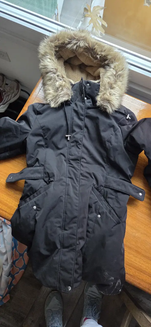 Campera negra de abrigo con capucha de piel sintética, ideal para el invierno. Posee cierre y bolsillos.