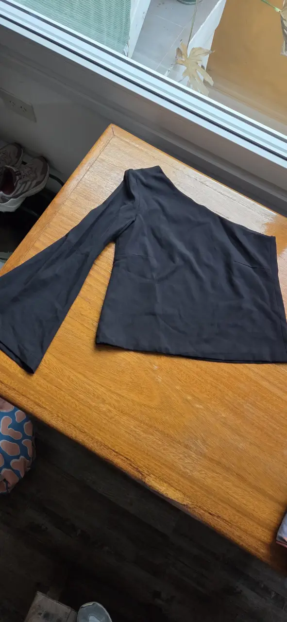 Blusa negra de un solo hombro con manga larga y corte asimétrico. Ideal para un look elegante y moderno.