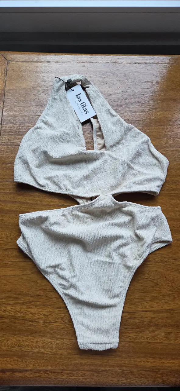 Traje de baño de una pieza color crudo. Top con diseño halter y abertura en el centro. La parte inferior es de corte alto. Ideal para la playa o pileta.