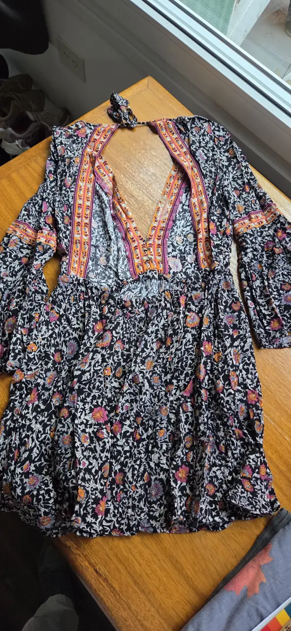 Vestido mini de estilo boho con estampado floral en tonos negro, rosa y naranja. Diseño con escote en V y mangas largas acampanadas. Ideal para un look casual y con onda.
