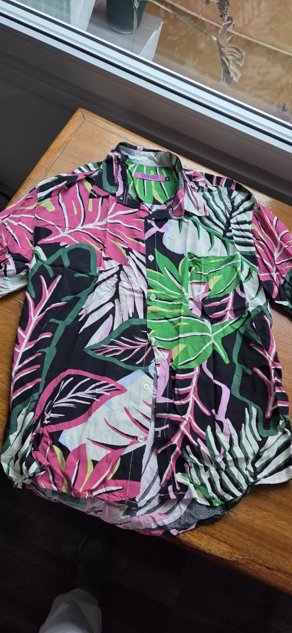 Camisa estampada con hojas en tonos rosa, verde y blanco sobre fondo negro. Ideal para un look casual y moderno.