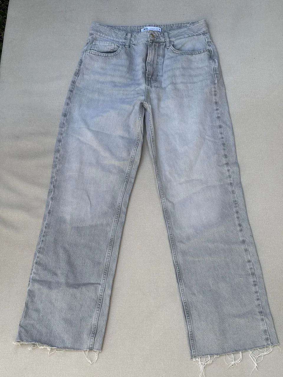 Jeans corte recto y ancho, con roturas desflecadas en los bajos. Color gris claro, con un lavado desgastado que le da un toque moderno y canchero. Ideales para un look casual y relajado.