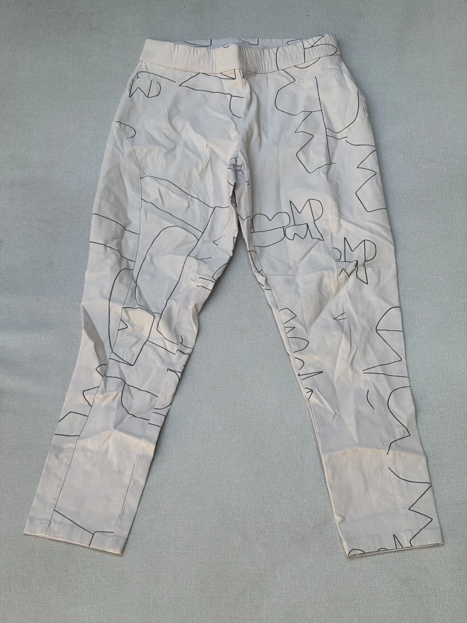 Pantalón de vestir tiro alto con estampa abstracta en negro sobre fondo crudo. Diseño moderno y original, ideal para un look canchero y único. Corte recto y cómodo.