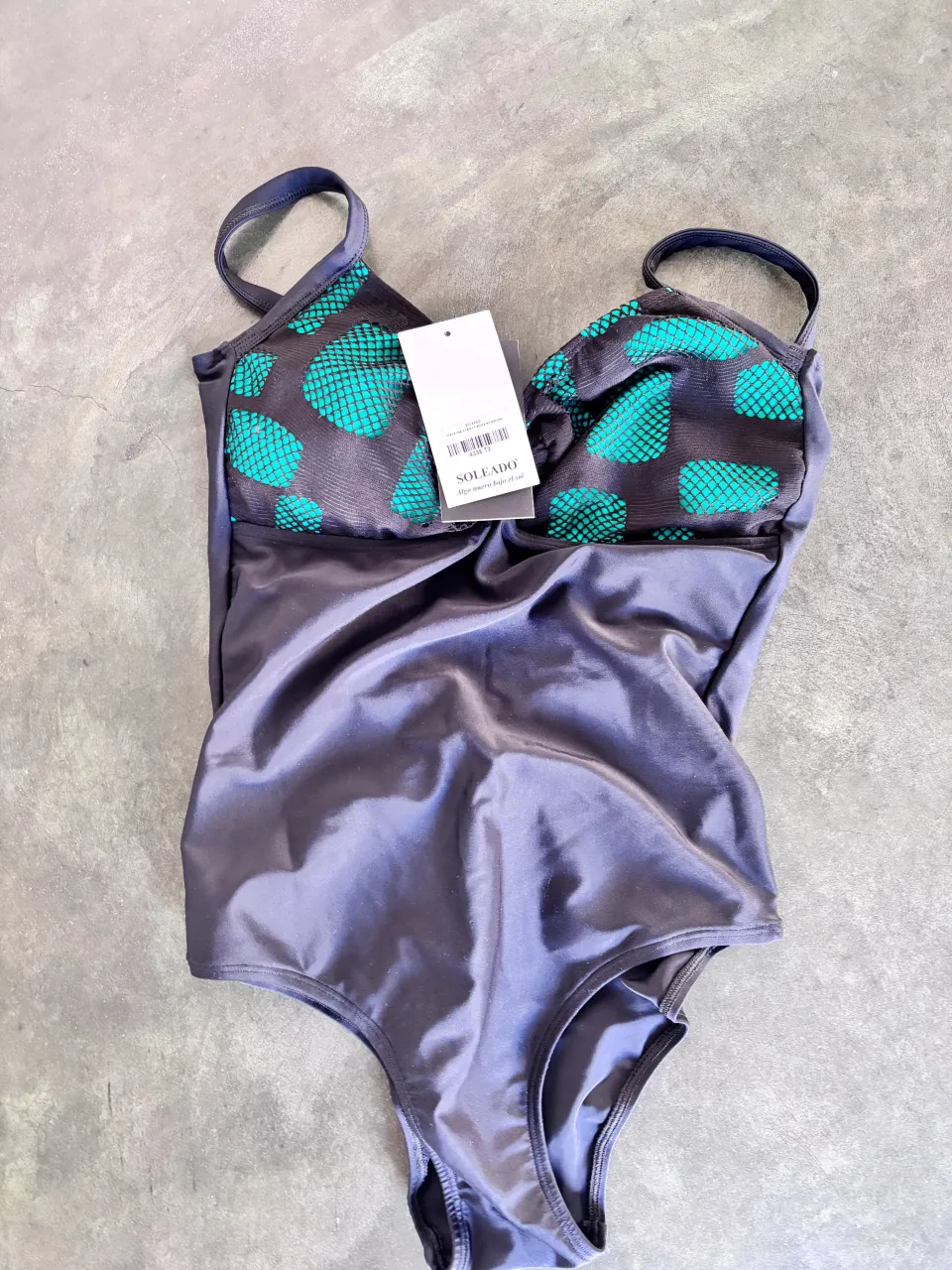 Traje de baño entero de color gris oscuro con estampado de puntos verde agua en la parte superior del busto. Breteles finos.