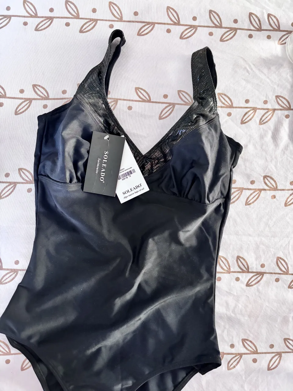 Traje de baño entero negro, con breteles anchos y detalle de textura en la parte superior del busto y breteles. Escote en V pronunciado en la espalda.