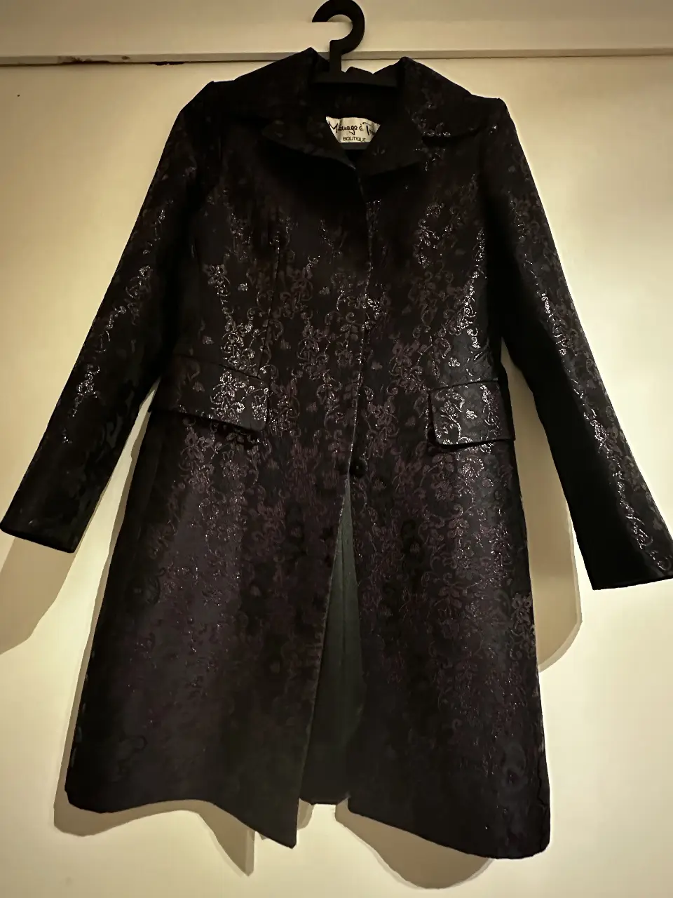 Tapado largo de mujer, negro con estampado floral en relieve. Corte elegante y sofisticado, ideal para ocasiones especiales. Confeccionado con un tejido de alta calidad, este abrigo ofrece un ajuste favorecedor y un estilo atemporal. Perfecto para completar cualquier look de invierno.