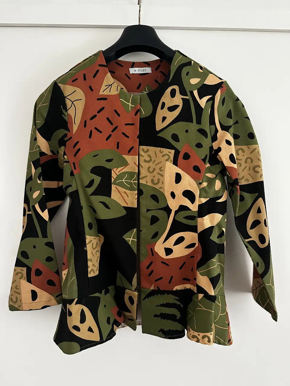 Blusa estampada con diseño de hojas y formas geométricas en tonos verdes, marrones y negros. Corte holgado y mangas largas con detalle de volado en los puños. Ideal para un look casual con un toque artístico.
