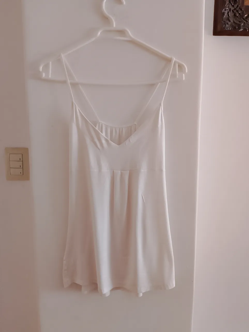 Remera blanca súper delicado y fresco, ideal para el verano. Tiene tiras finas y un escote en V con detalles de pliegues que le dan un toque especial. Es perfecto para una salida casual.
