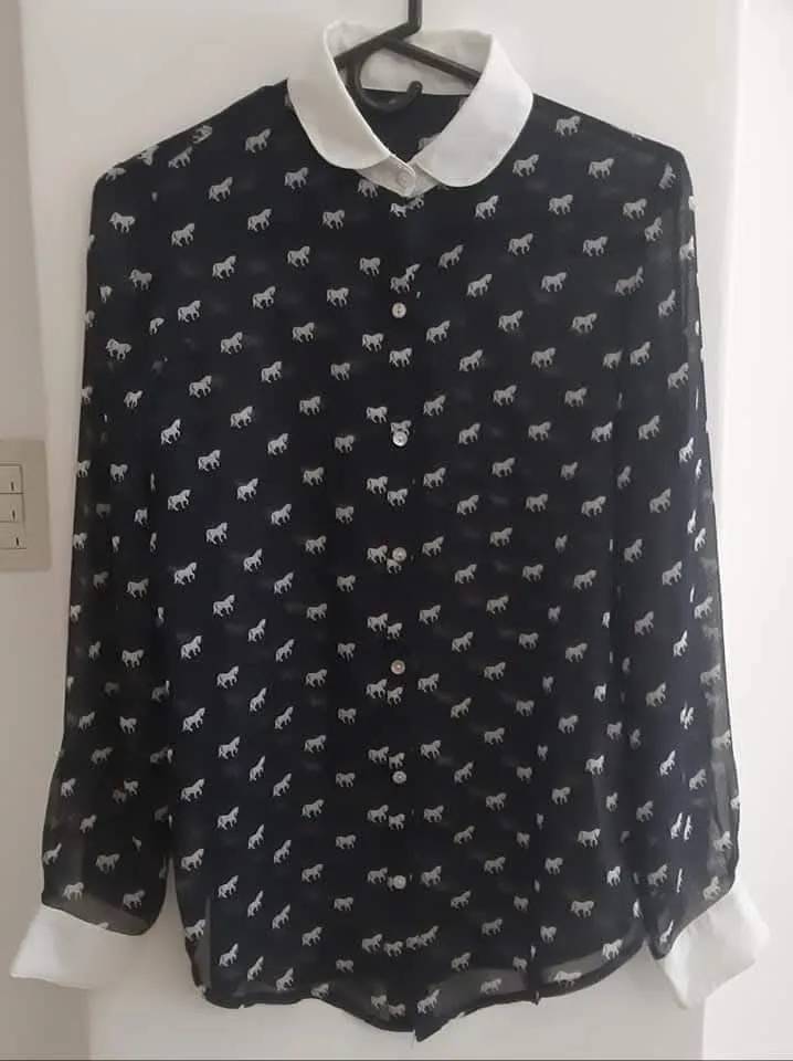 Blusa de mujer con estampado de caballos en color blanco sobre fondo azul. Cuello y puños blancos. Ideal para un look elegante y sofisticado.