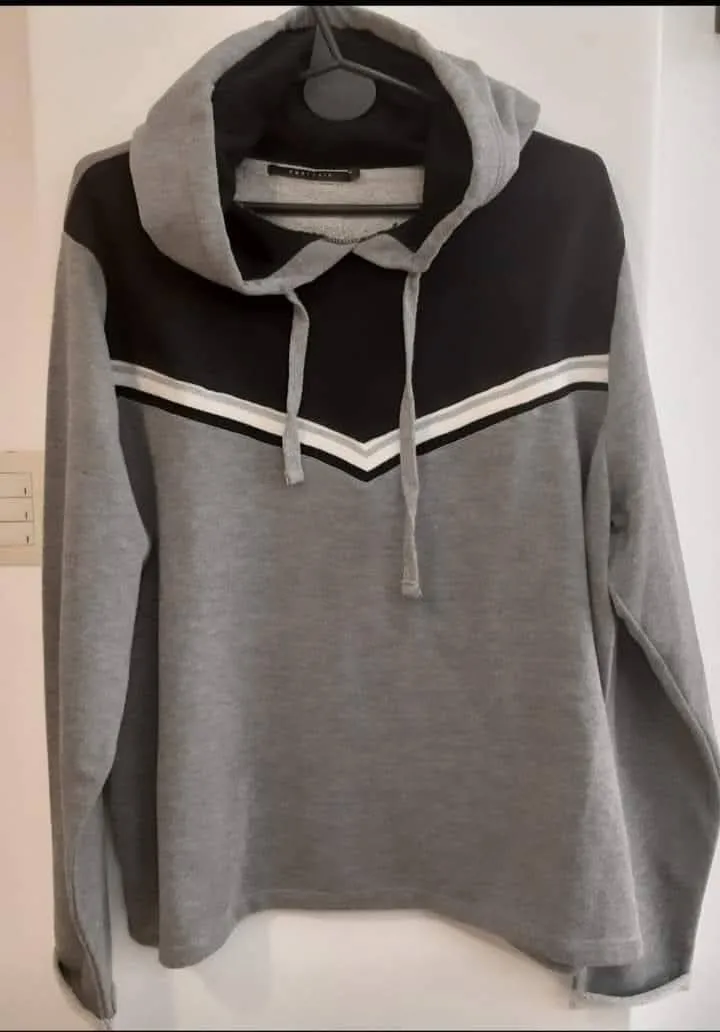 Buzo Portsaid, con capucha y diseño en color gris y negro. Detalles en blanco y plateado en el frente. Ideal para un look casual y cómodo.