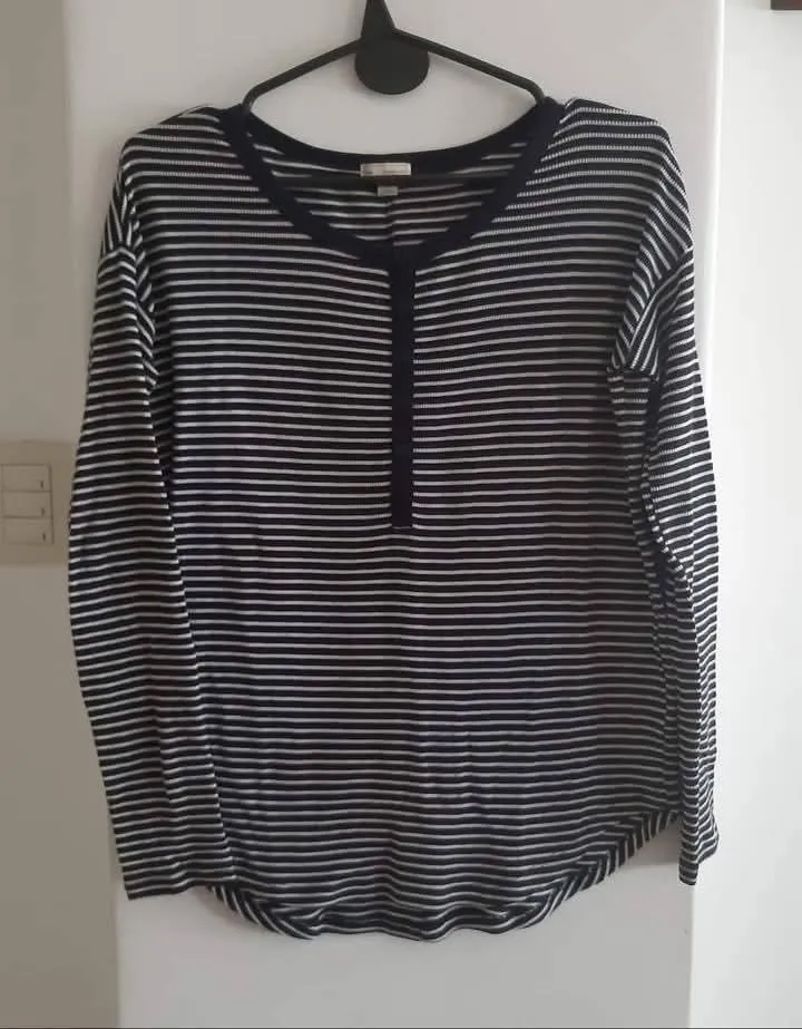 Remera de manga larga a rayas horizontales en blanco y azul marino. Tiene un cuello redondo y una tapeta con botones en el frente. Ideal para un look casual y cómodo.