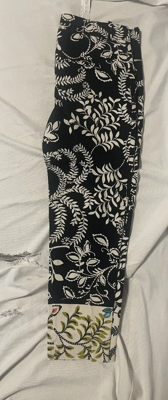 Pantalón sastrero de mujer, estampado con hojas blancas sobre fondo negro. Detalles en la parte inferior con diseño floral. Marca Zara.