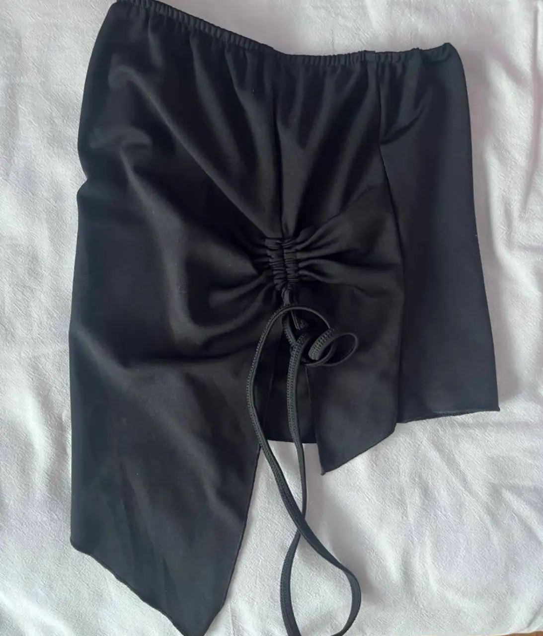 Top asimétrico negro con detalle fruncido y cordón. Ideal para un look de fiesta.