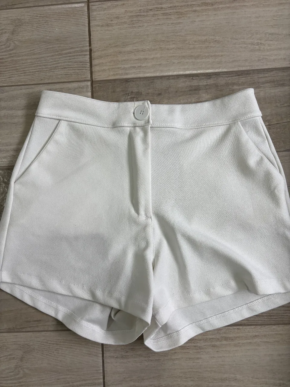 Short blanco, con bolsillos delanteros y cierre. Ideal para un look elegante y moderno.