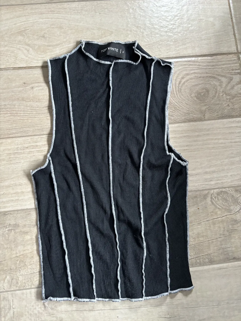 Top negro con costuras blancas a la vista. Diseño con cuello alto y sin mangas. Ideal para un look moderno y versátil.