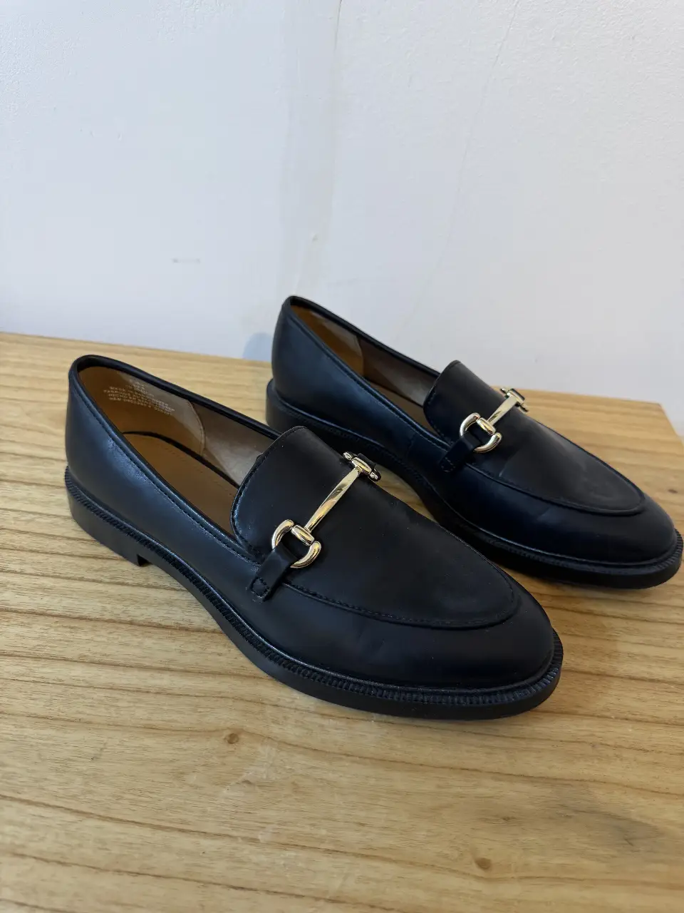 Mocasines negros de cuero con detalle dorado. Tienen un diseño clásico y elegante, ideales para un look formal o casual.
