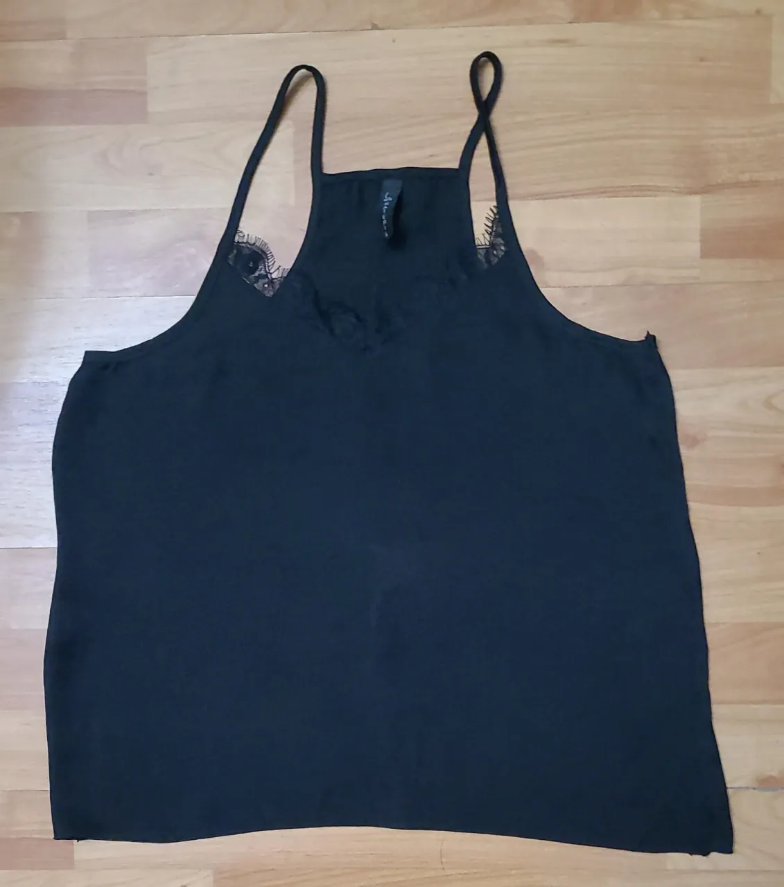 Top negro con detalles de encaje en el escote y tirantes finos. Ideal para combinar con diferentes outfits, desde looks casuales hasta más elegantes.