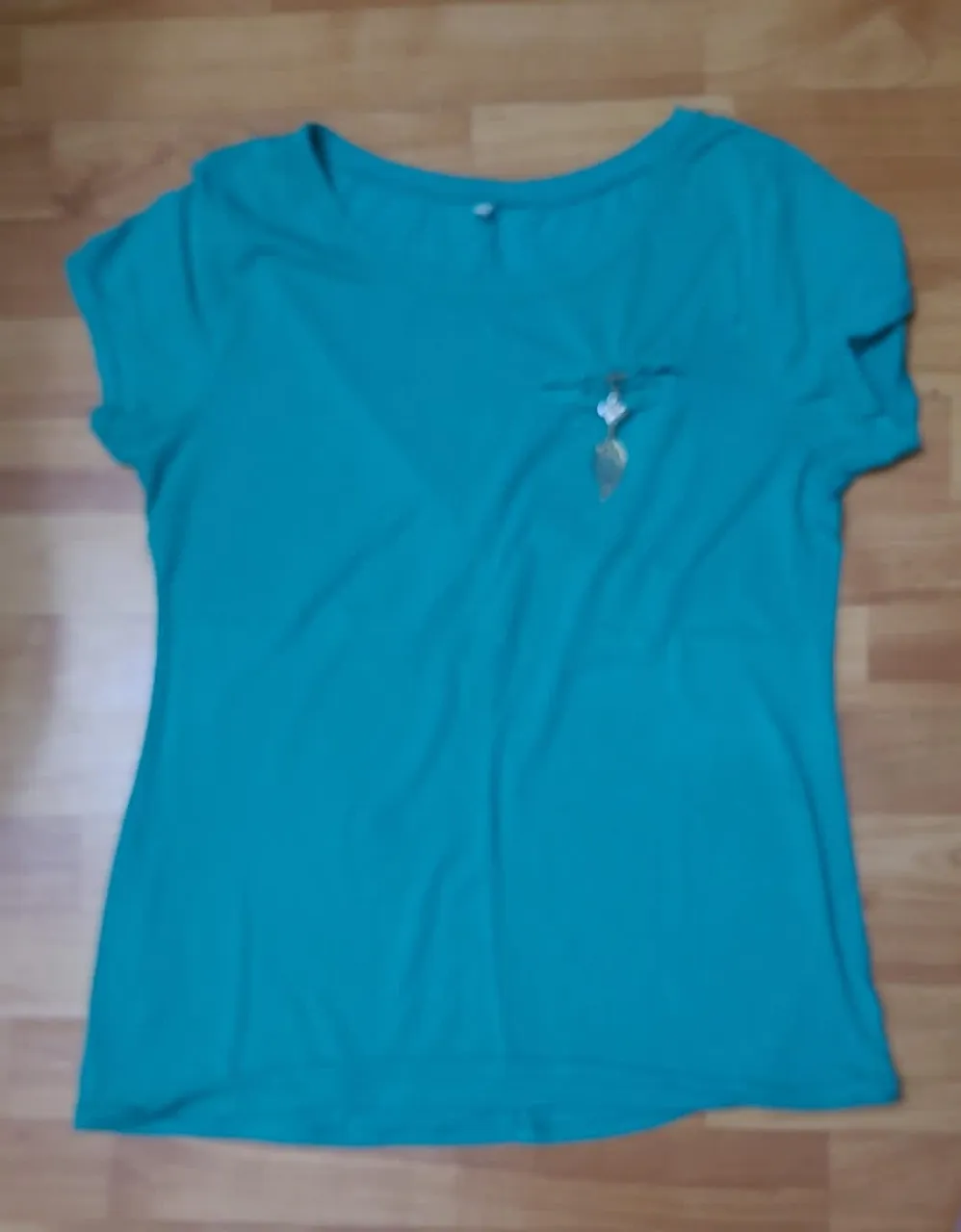 Remera de mujer de color verde, con detalle de dije dorado en el frente. Ideal para un look casual y fresco.
