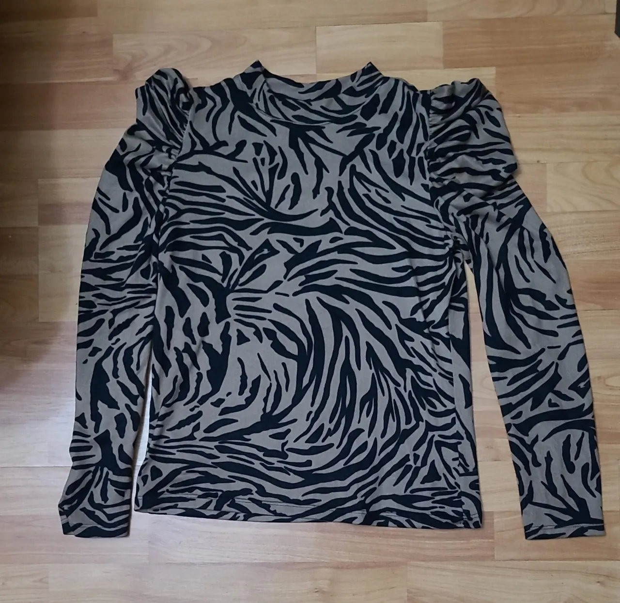 Blusa de mujer con estampado de cebra en tonos negro y crudo. Diseño con mangas largas y detalle de hombros abullonados, cuello alto. Ideal para un look moderno y sofisticado.