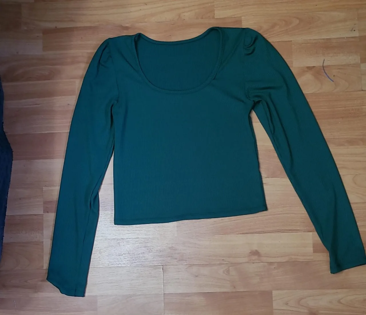Remera de manga larga para mujer, de color verde oscuro. Confeccionada en tejido de punto acanalado, con cuello redondo y mangas con detalle de hombro fruncido. Ideal para un look casual y moderno.