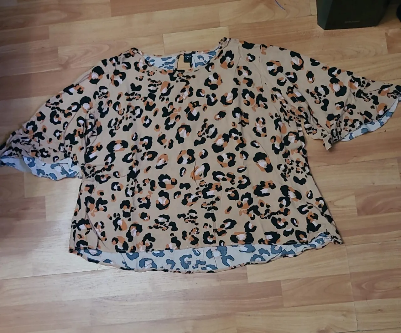 Blusa de mujer con estampado de leopardo en tonos beige y negro. Manga corta con volados y cuello redondo. Ideal para un look casual y moderno.
