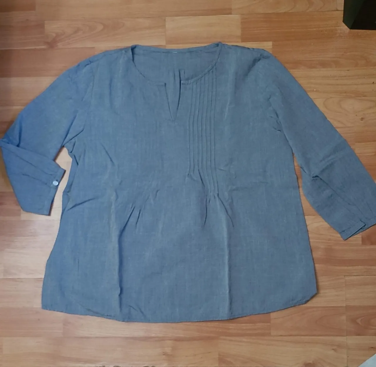 Blusa de manga 3/4 gris con detalle de pliegues en el frente y cuello en V. Ideal para un look casual y cómodo.