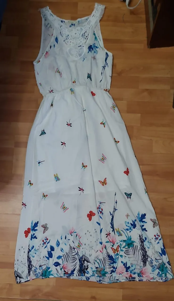 Vestido largo de mujer, blanco con estampado floral y de mariposas. Tiene detalles de encaje en el escote y cintura elastizada. Ideal para un look fresco y primaveral.