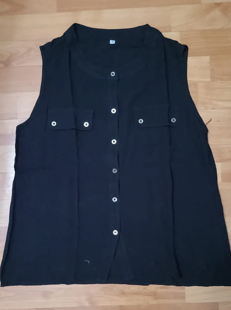 Blusa sin mangas de color negro, con botones frontales y dos bolsillos delanteros. Ideal para un look casual y versátil.