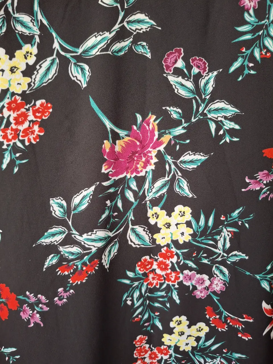 Blusa estampada con flores en tonos rojos, amarillos y rosas sobre fondo negro. Ideal para un look femenino y con estilo.