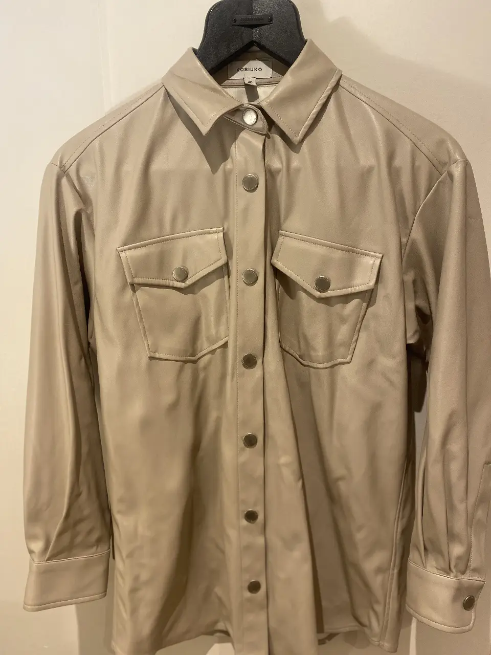 Camisa de cuero sintético color crudo, con dos bolsillos delanteros y botones plateados. Ideal para un look moderno y sofisticado.