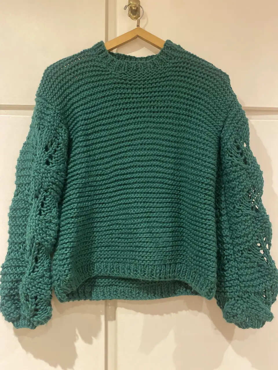 Sweater de punto grueso color verde, con mangas abullonadas y detalles calados. Cuello redondo y ajuste holgado. Ideal para un look casual y abrigado.