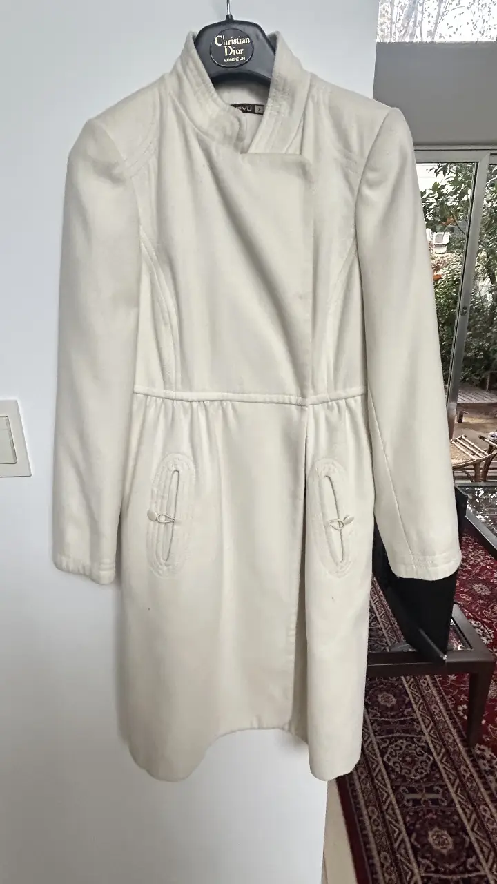 Tapado largo de color blanco, con diseño elegante y detalles únicos. Posee bolsillos delanteros con un detalle decorativo y un corte que estiliza la figura. Ideal para un look sofisticado y abrigado.