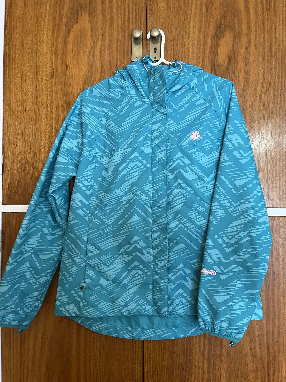 Campera rompevientos Mountain Gear para mujer, talle XL. Diseño con estampado geométrico en tonos celeste/verdosos y detalles en rosa. Impermeable y con capucha.