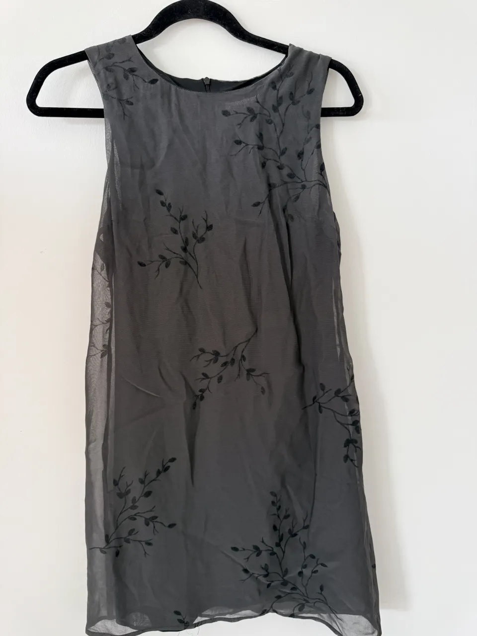 Vestido gris oscuro con delicado estampado de ramitas en negro. Diseño sin mangas y largo hasta la rodilla, ideal para un look elegante y sutil. Perfecto para eventos o salidas.