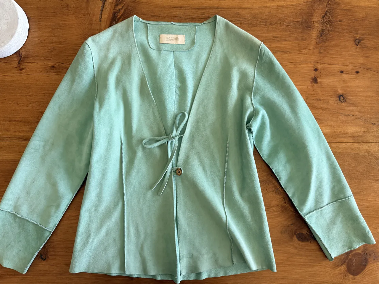Chaqueta de gamuza verde menta, con escote en V y lazo para atar. Mangas largas con detalle desflecado. Ideal para un look boho chic o casual.