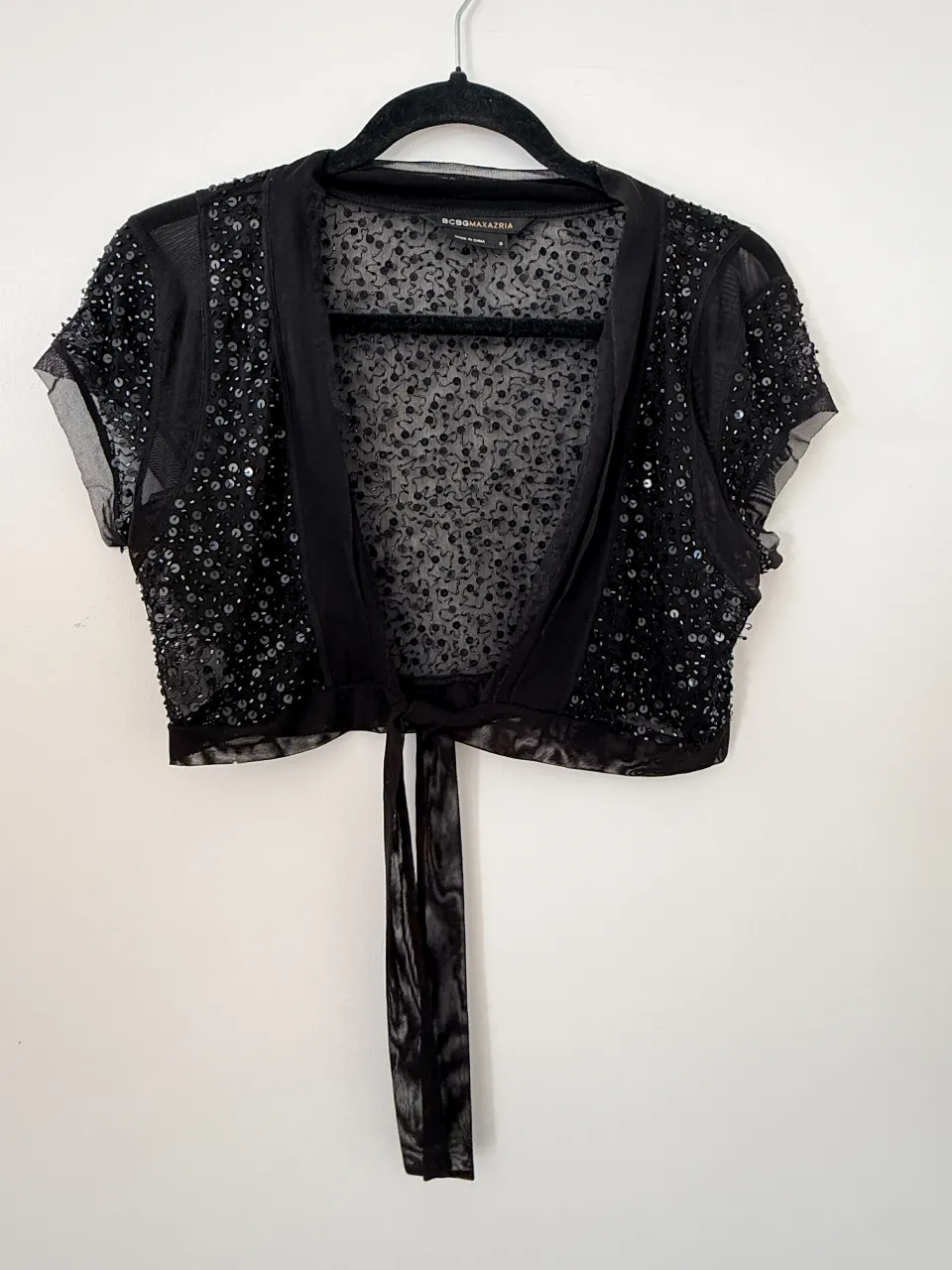 Bolero negro con brillos y detalles de lentejuelas. Posee mangas cortas y se ata al frente con un lazo. Ideal para complementar outfits de fiesta o noche.