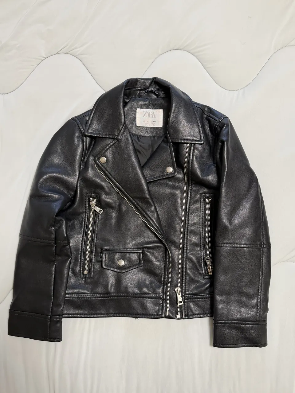 Campera de cuero sintético negra con cierre metálico al frente, bolsillos con cierre en los laterales y un bolsillo con botón a presión en el frente. Cuello solapa.